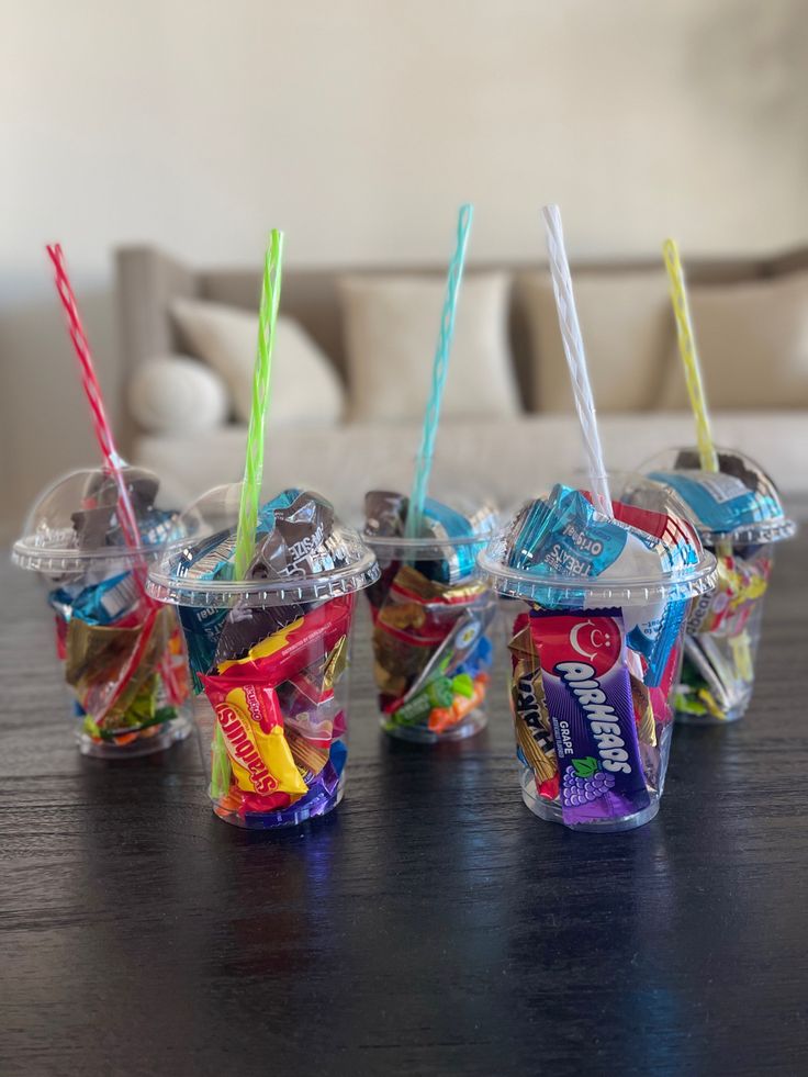 four plastic cups filled with candy and drinking straws on top of a wooden table