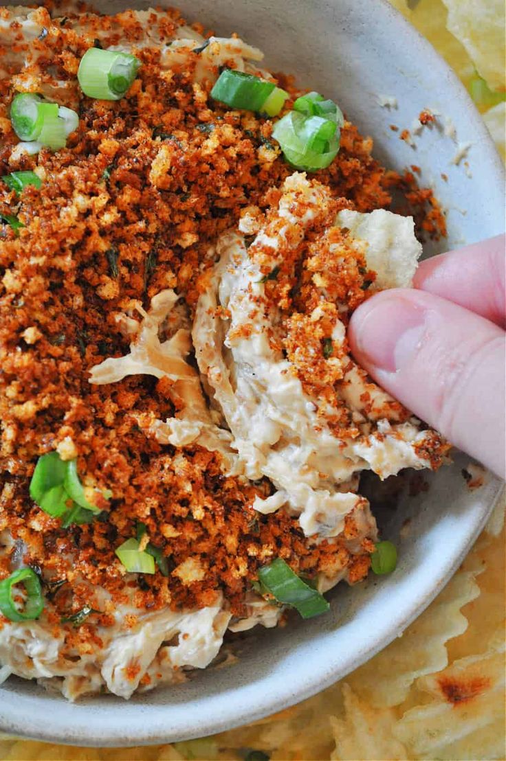 someone is holding their hand up to a bowl full of food that includes rice and green onions