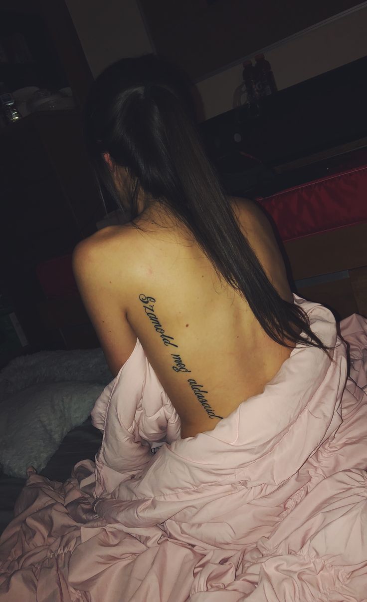 a woman with a tattoo on her back sitting in a pink dress and looking off into the distance