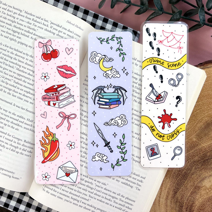 two bookmarks with designs on them sitting next to an open book