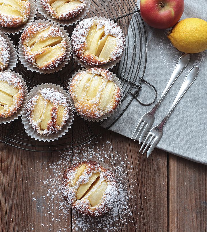 some desserts are sitting on a plate with powdered sugar and an apple in the background