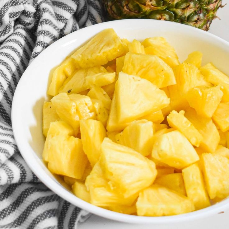 a white bowl filled with sliced pineapple next to a black and white dish towel