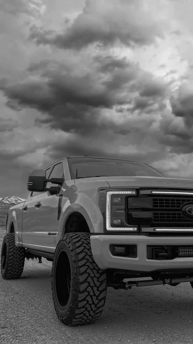 a white truck parked on top of a parking lot next to a mountain covered in clouds