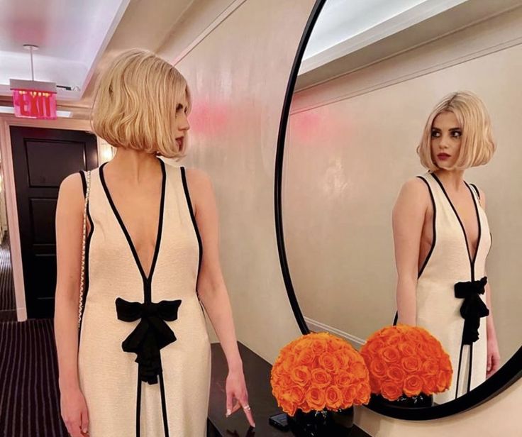 a woman standing in front of a mirror holding an orange flower bouquet and looking at herself in the mirror