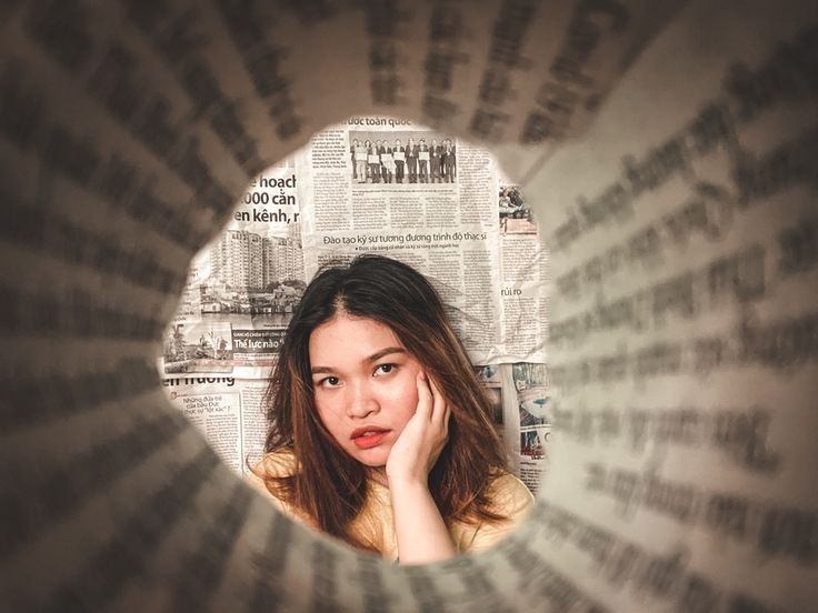 a woman is looking through a hole in the newspaper with her hand on her face