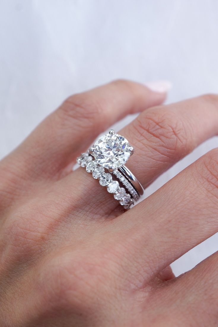 a woman's hand with a diamond ring on top of her finger and the other hand holding an engagement ring