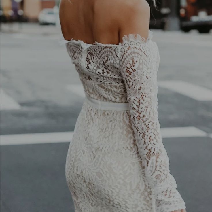 a woman in a white dress is standing on the street with her back to the camera