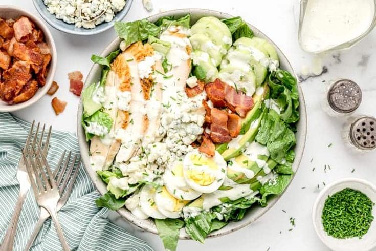 a salad with bacon, lettuce and dressing in bowls next to other ingredients