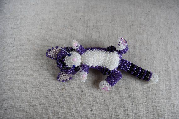 a purple and white beaded cat laying on top of a gray surface with it's eyes closed