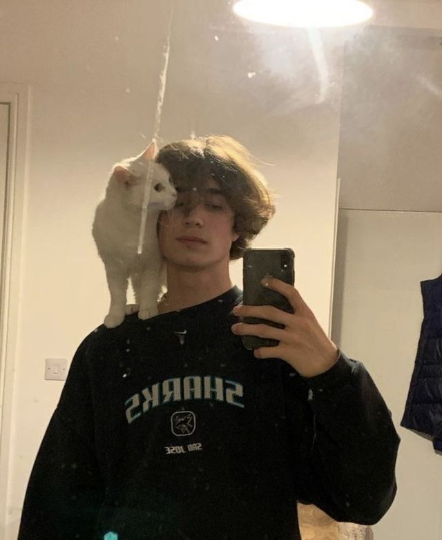 a man taking a selfie in front of a mirror with a cat on his shoulder