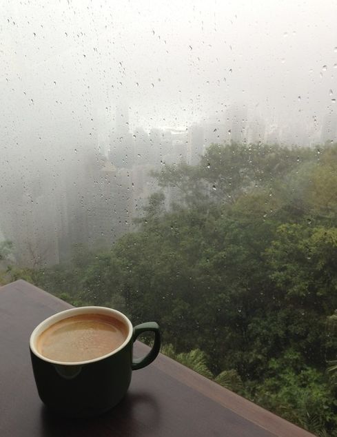 a cup of coffee sitting on top of a table next to a window covered in rain