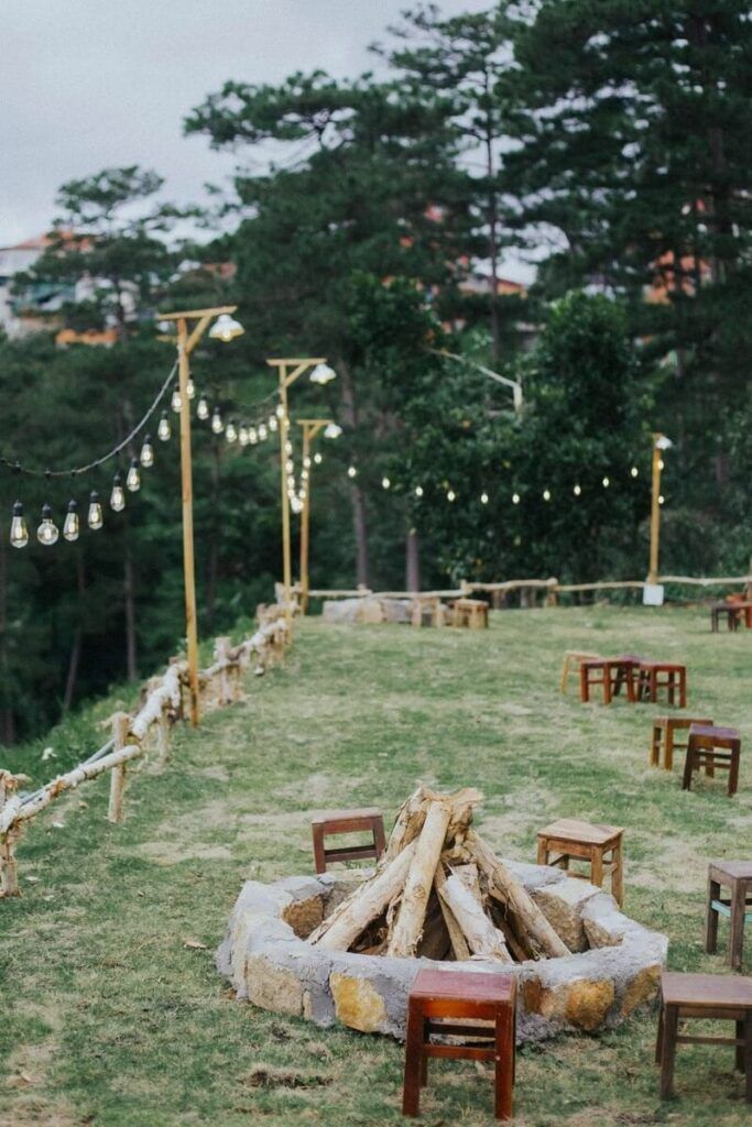 a fire pit surrounded by wooden chairs and string lights in the middle of a field