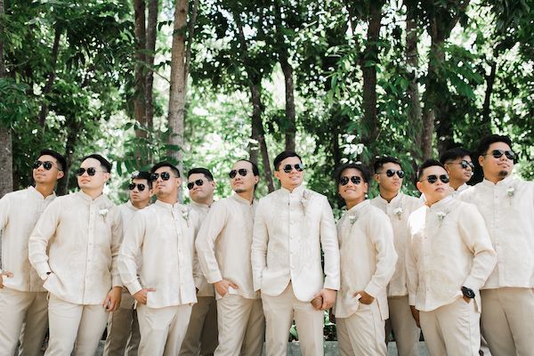 a group of men in white suits and sunglasses standing next to each other with trees behind them