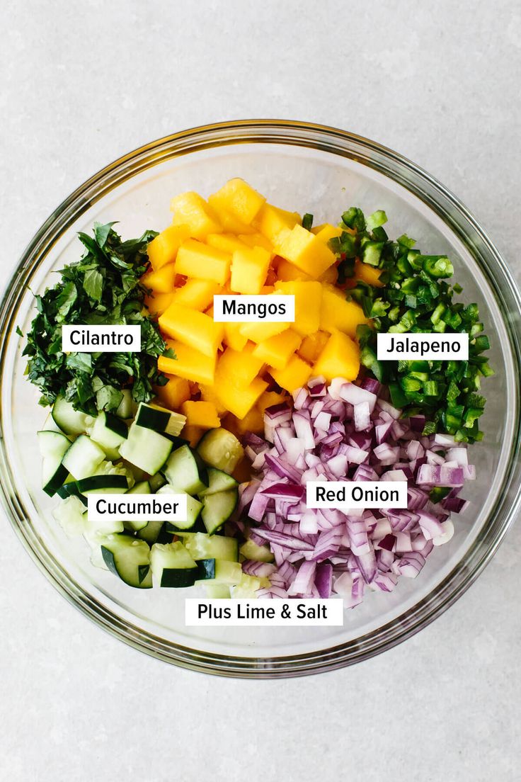 the ingredients for this salad are in a glass bowl, including onions, cucumber, red onion, and mango