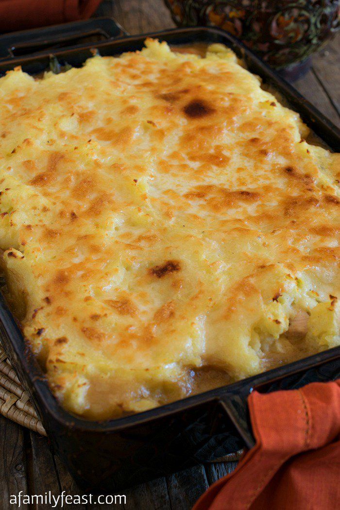 a casserole dish with cheese on top in a black pan and an orange napkin next to it