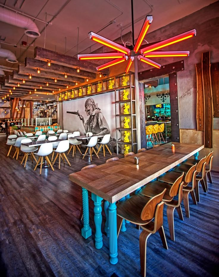 a restaurant with wooden tables and chairs in front of a large painting on the wall