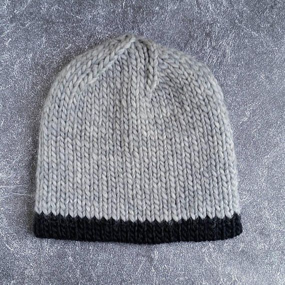 a white and black knitted beanie hat sitting on top of a gray surface