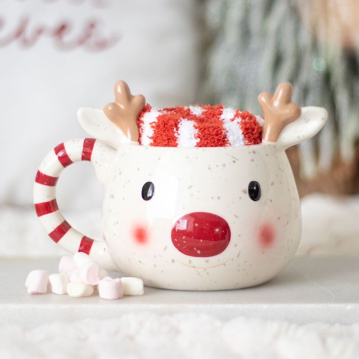 a cup with some candy in it and a reindeer face on the inside is sitting next to marshmallows