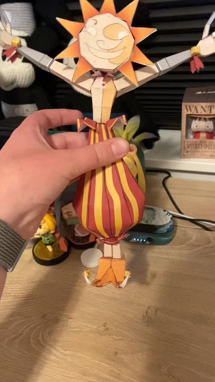 a person is holding up a paper doll on a wooden table with other toys in the background