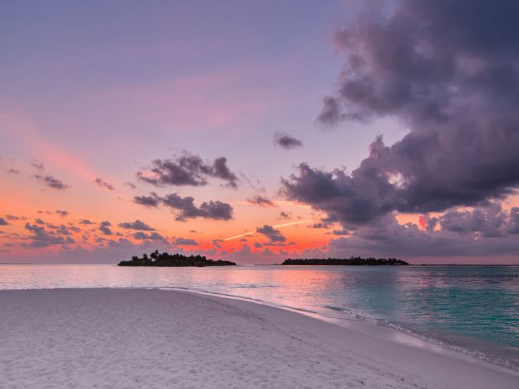 the sun is setting over an island in the ocean with sand and water on both sides