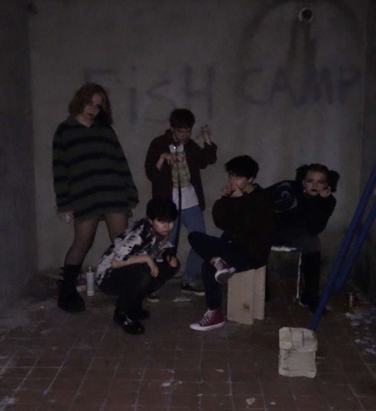 group of young men sitting on stools in an empty room with graffiti written on the wall