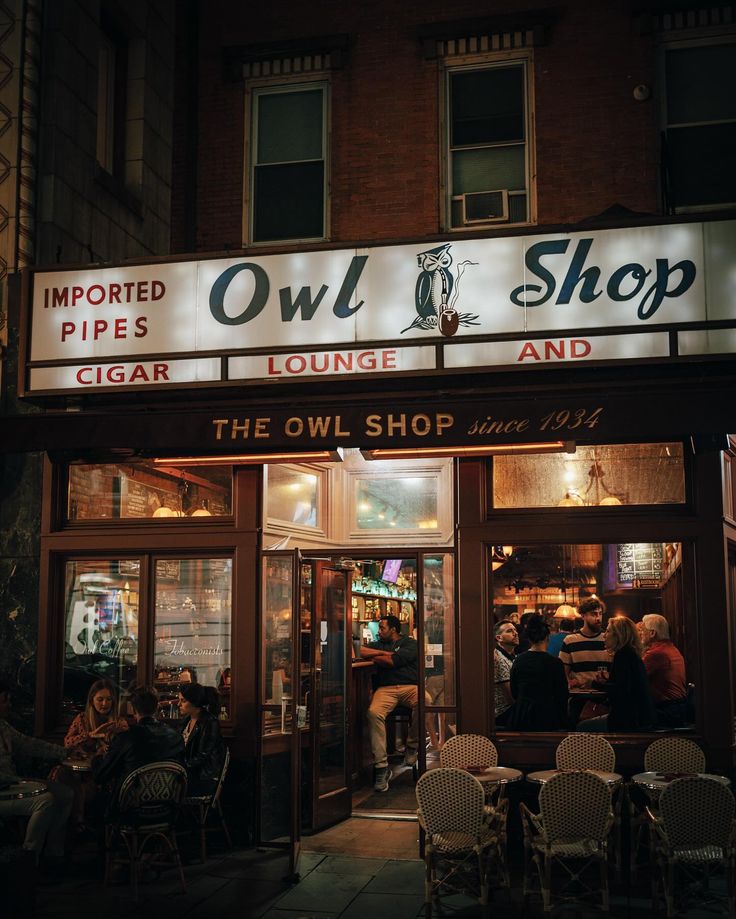 the entrance to owl shop at night with people sitting in chairs and tables outside it