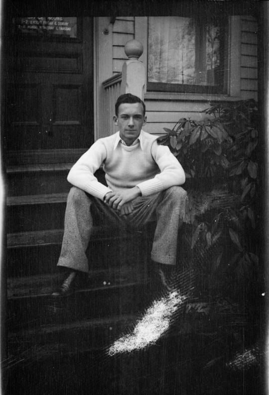 black and white photograph of a man sitting on the steps in front of a house