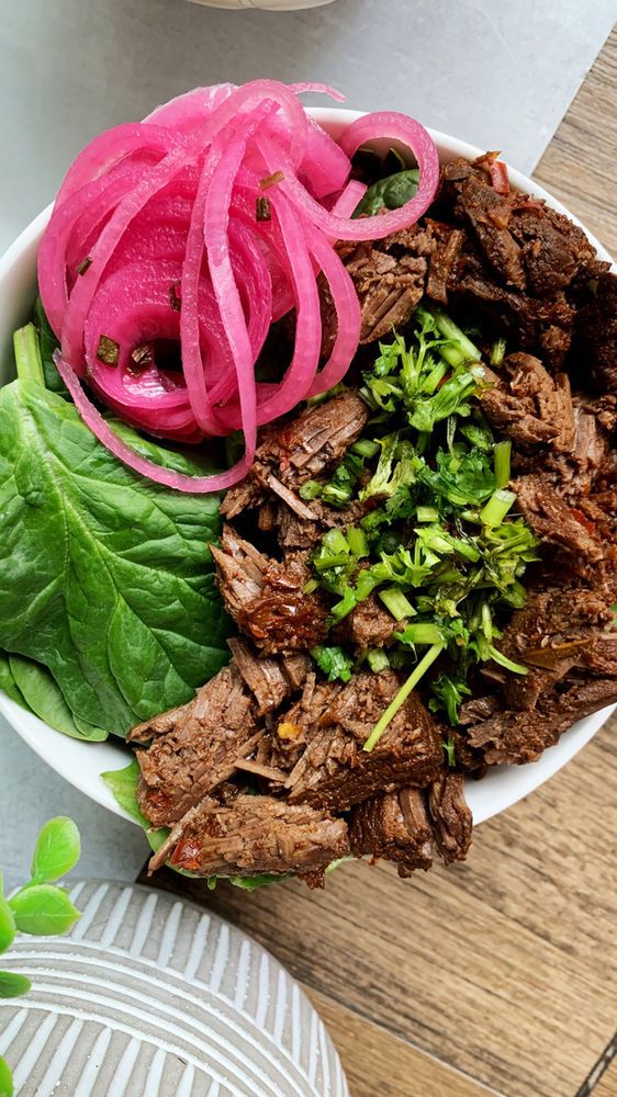 a white bowl filled with meat and veggies on top of a wooden table