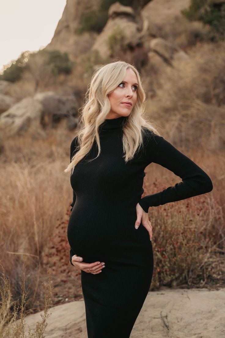 a pregnant woman standing in the desert wearing a black dress