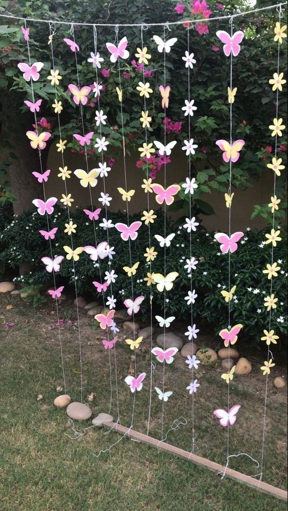 some paper butterflies hanging from a wire in front of a bush with rocks and grass