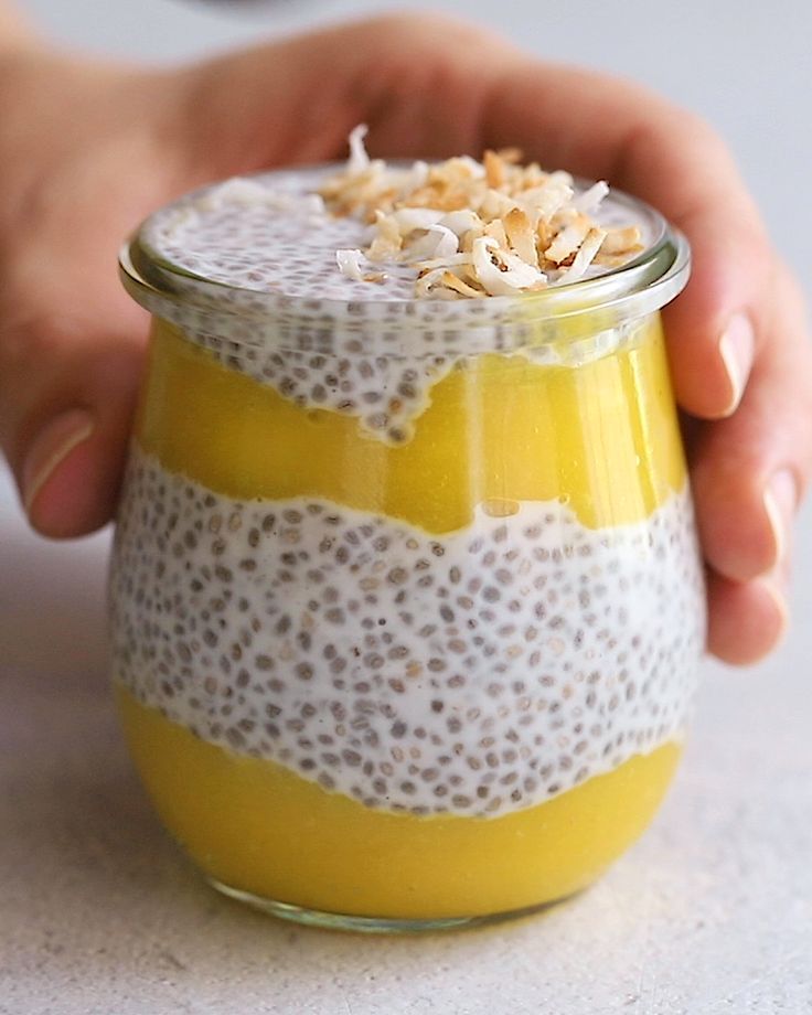 a person is holding a small glass jar filled with food and garnished with coconut flakes