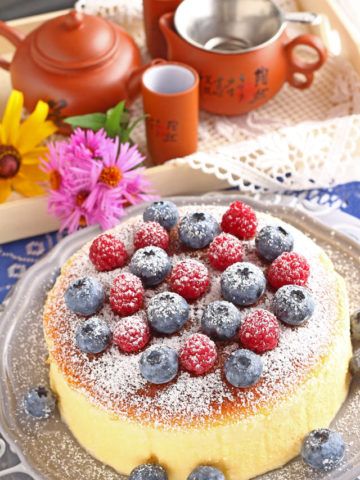 a cake with berries and powdered sugar on top sitting on a plate next to teapots