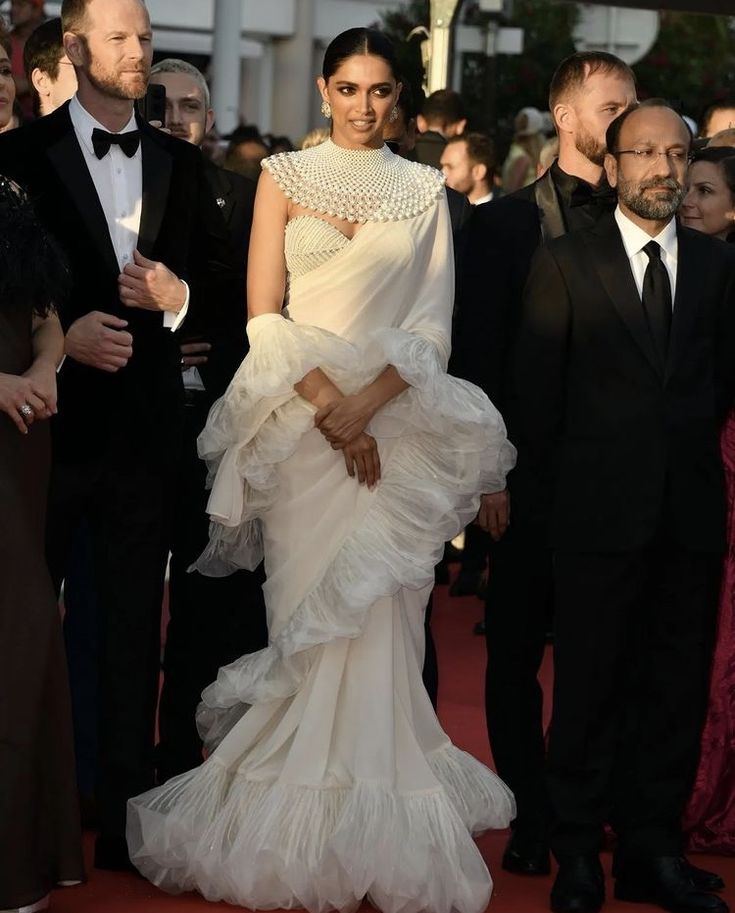 a woman in a white gown standing on a red carpet with other people around her