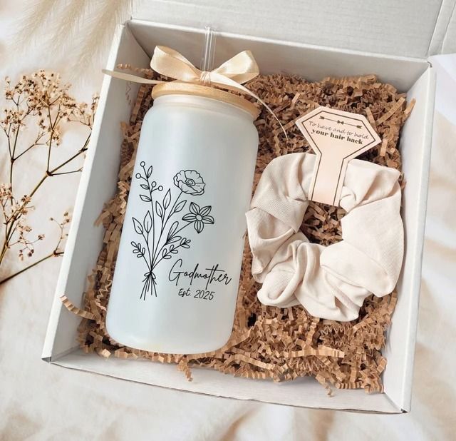 an open gift box containing a white bottle with flowers on it and a ribbon tied around the top