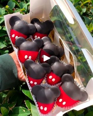 a box filled with lots of cupcakes covered in mickey mouse icing on top of green leaves