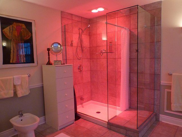 a bathroom with a shower, toilet and sink in it's center area is lit up by red lights