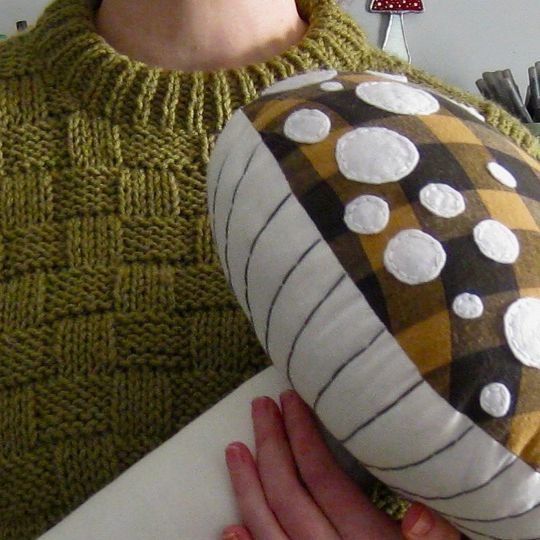 a woman is holding a decorative object in her hands and wearing a green sweater with white polka dots on it