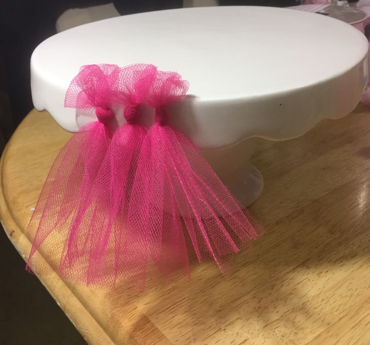 a white cake with pink ribbons on it sitting on top of a wooden table next to other cakes