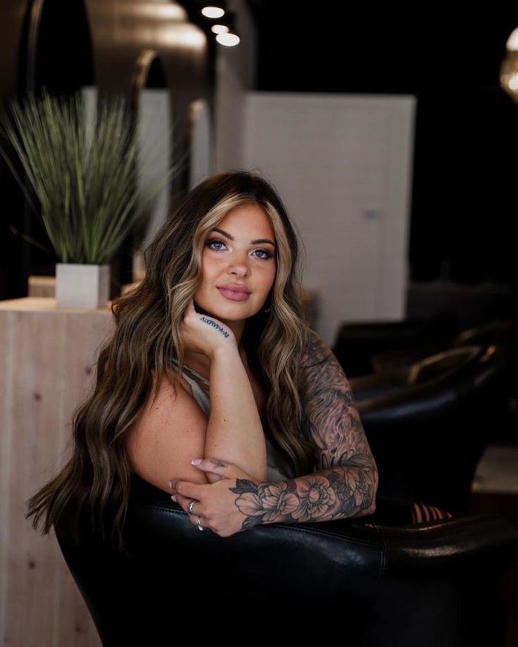 a woman sitting in a black chair with tattoos on her arm and arms behind her head