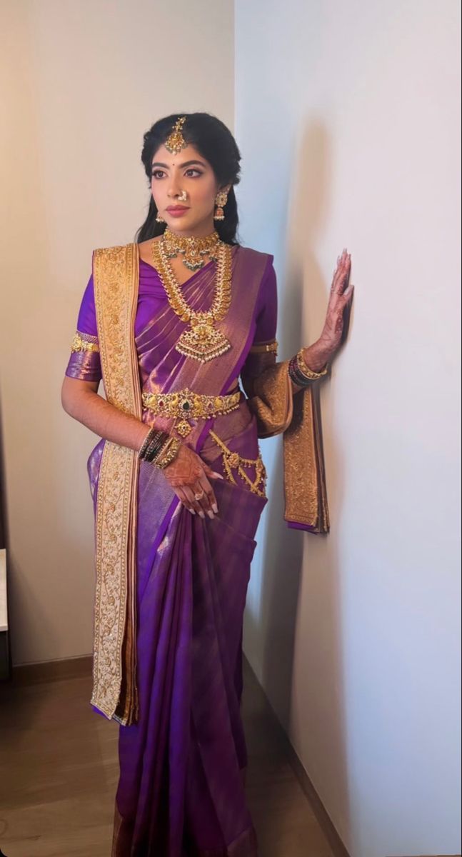 a woman in a purple and gold sari standing next to a wall with her hand on