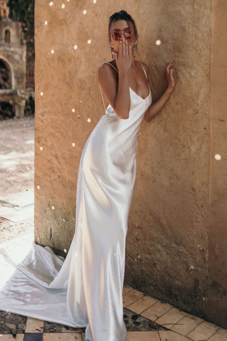 a woman in a white dress leaning against a wall with her hand on her face