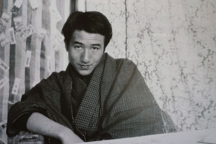 a black and white photo of a man wearing a kimono sitting at a table