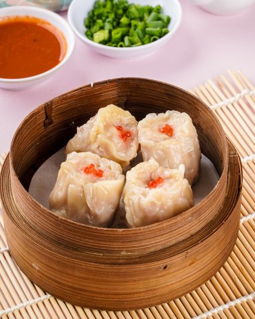 some dumplings are in a wooden bowl on a table with bowls of vegetables and sauces