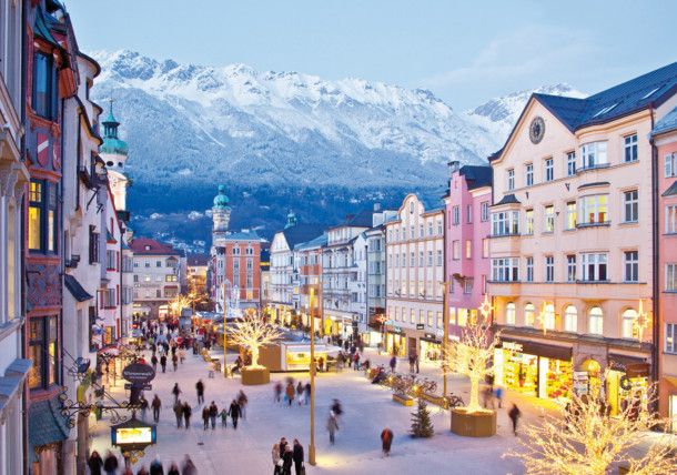 people are walking down the street in front of buildings with snow covered mountains behind them