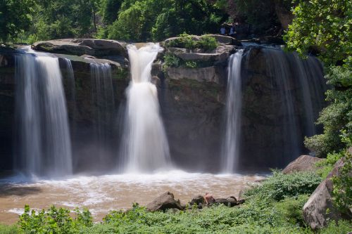 a waterfall with a bridge over it and people standing at the bottom in the water