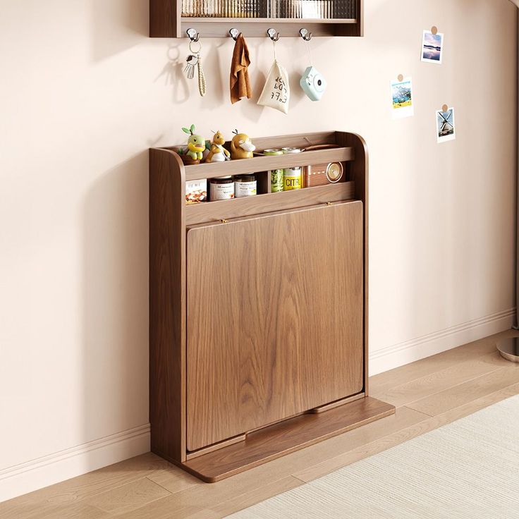 a wooden cabinet sitting in the corner of a room next to a wall with hooks and magnets on it