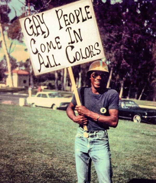 a man holding a sign that says gay people come in all colors