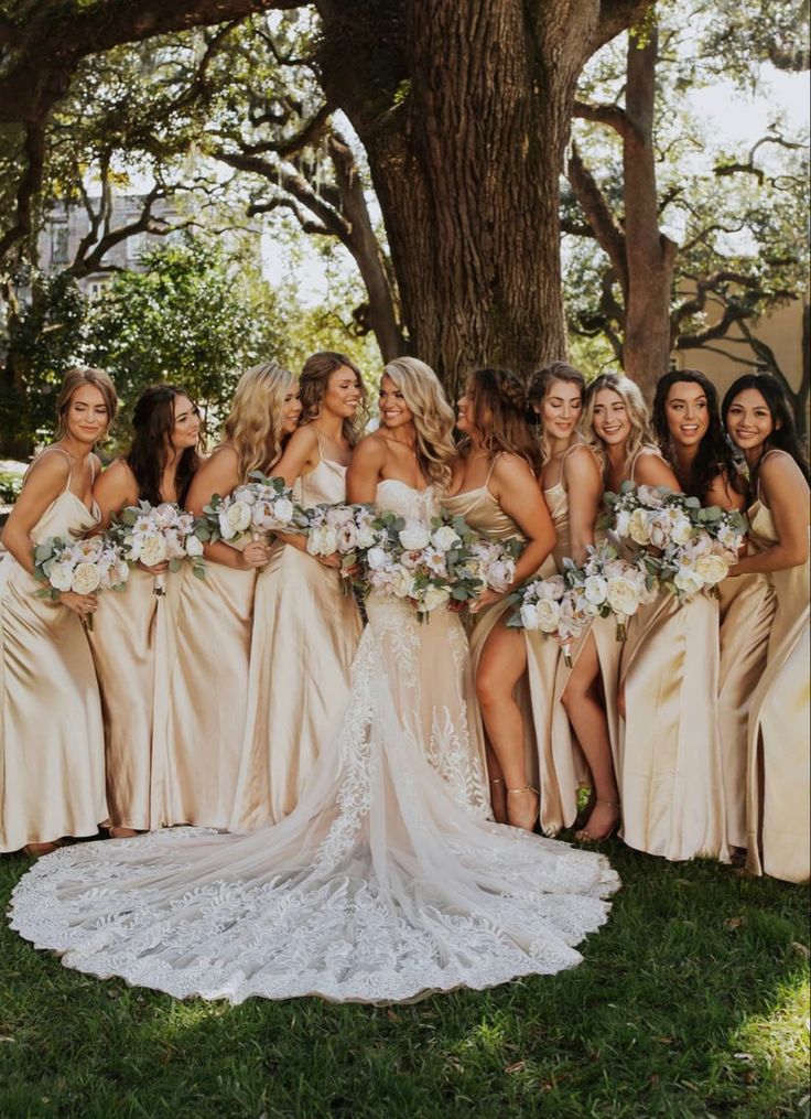 a group of women standing next to each other in front of a tree with bouquets