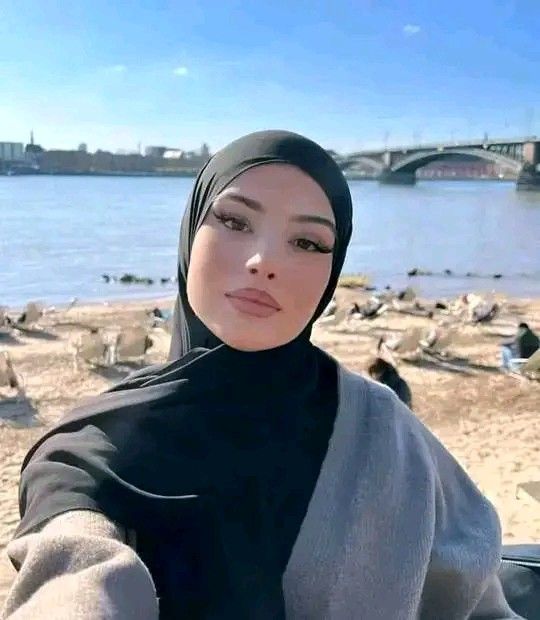 a woman wearing a hijab is taking a selfie on the beach with seagulls in the background