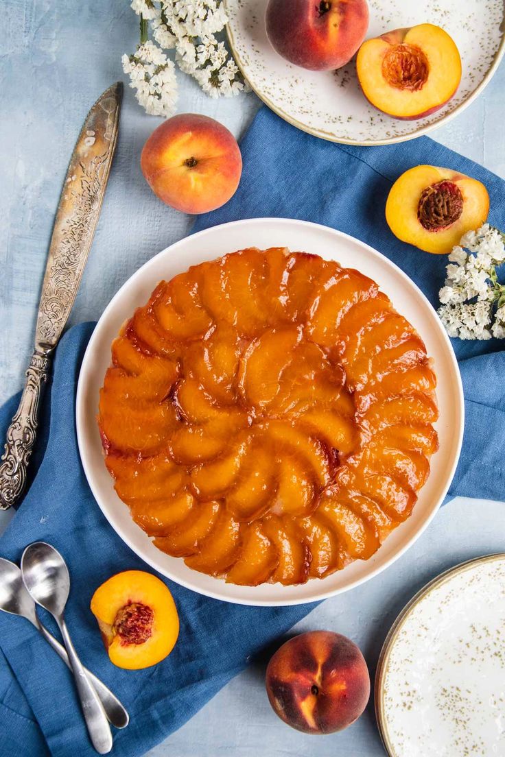 a bowl filled with sliced peaches next to plates and spoons on a blue cloth